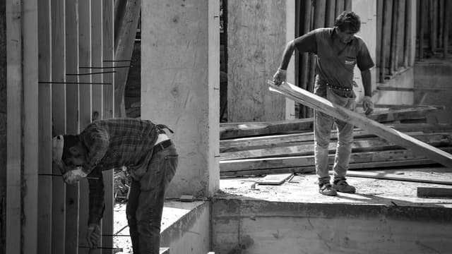 Deux ouvriers sur un chantier de gros œuvre, entre poteaux en béton et coffrages