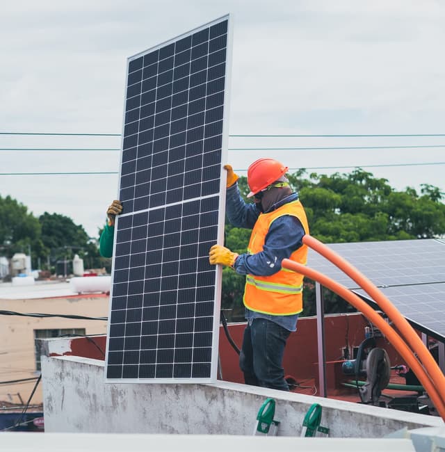 Installateur casqué posant un panneau photovoltaïque sur un toit